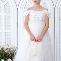 A teenager standing in a white, floral dress with a high neckline, long sleeves, and an open back, in a setting with a decorative arch in the background.