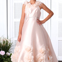 A young girl in a salmon pink flower girl's dress with intricate floral embroidery, posing in a room with white doors and a decorative plant.