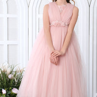 A little girl in a soft pink flower girl's dress with delicate lace detailing and a full tulle skirt, standing in a beautifully decorated room.