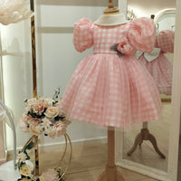 A pink checkered girls' dress with short puffed sleeves and a knee-length skirt displayed on a mannequin.