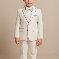 A young boy wearing a white suit with a matching pants paired with a bow tie and black shoes.