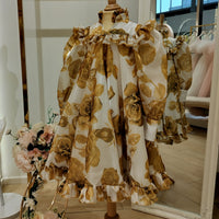 A yellow long sleeve girls occasion dress with floral patterns displayed on a mannequin.