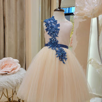 A sleeveless girls' dress with a satin bodice, sheer shoulders, lace, and crystal cut beads, sequin, and pearls. The skirt is multicolor and the dress has a V cut back.