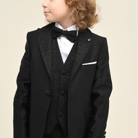 A boy wearing a black tuxedo with a bow tie and white shirt.