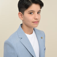 A boy wearing a blue suit with a white shirt, standing against a beige background.
