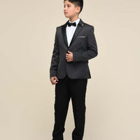 A boy wearing a black tuxedo with a bow tie and white shoes.