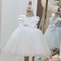 A white baby ivory dress with floral hair band, displayed on a mannequin with a reflective background.