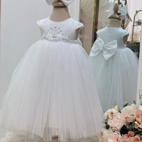 A baby white dress with floral embellishments on the waist, short sleeves, and a full tulle skirt, accompanied by a flower hair band, displayed in a retail setting.