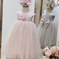A baby pink dress with a tulle skirt and delicate flowers on the waist, complemented by a flower hair band, displayed on a mannequin.