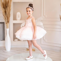 A young girl in a pink ballet dress with a flared skirt and embellished bodice, standing on a round platform.