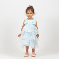 A toddler wearing a blue ruffled girls' dress with a polka-dot design, standing against a white background.