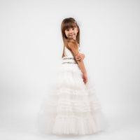 A young girl wearing a white tulle dress with a train, featuring pearl, beaded, and rhinestone detailing, in a studio setting.
