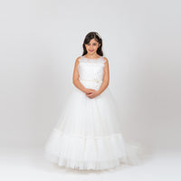 A young girl wearing a white dress with a satin bodice, flower lace, and tulle skirt, sleeveless with a V cut back, in a studio setting.