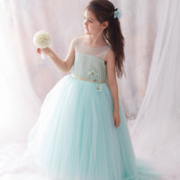 A young girl wearing a sleeveless, floor-length aqua blue dress with a sheer bodice covered in lace and embellishments.