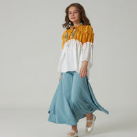 A young female model wearing a blue luxury pant set with a matching top, standing against a white background.