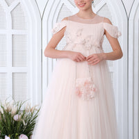 A teenage girl in a salmon-colored dress with a flowy silhouette and intricate floral pattern, standing in a room with a white, ornate background.