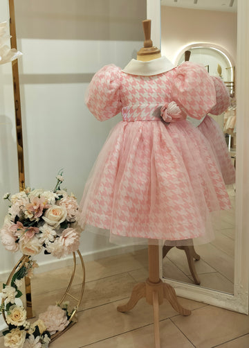 A pink girls' dress with a flowy skirt and a fitted bodice, displayed on a mannequin, with decorative flowers.
