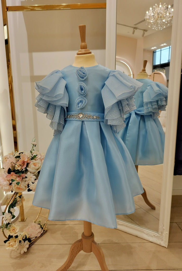 A sky blue girls' luxury dress with intricate lace detailing and a bow embellishment, displayed on a mannequin in a store.