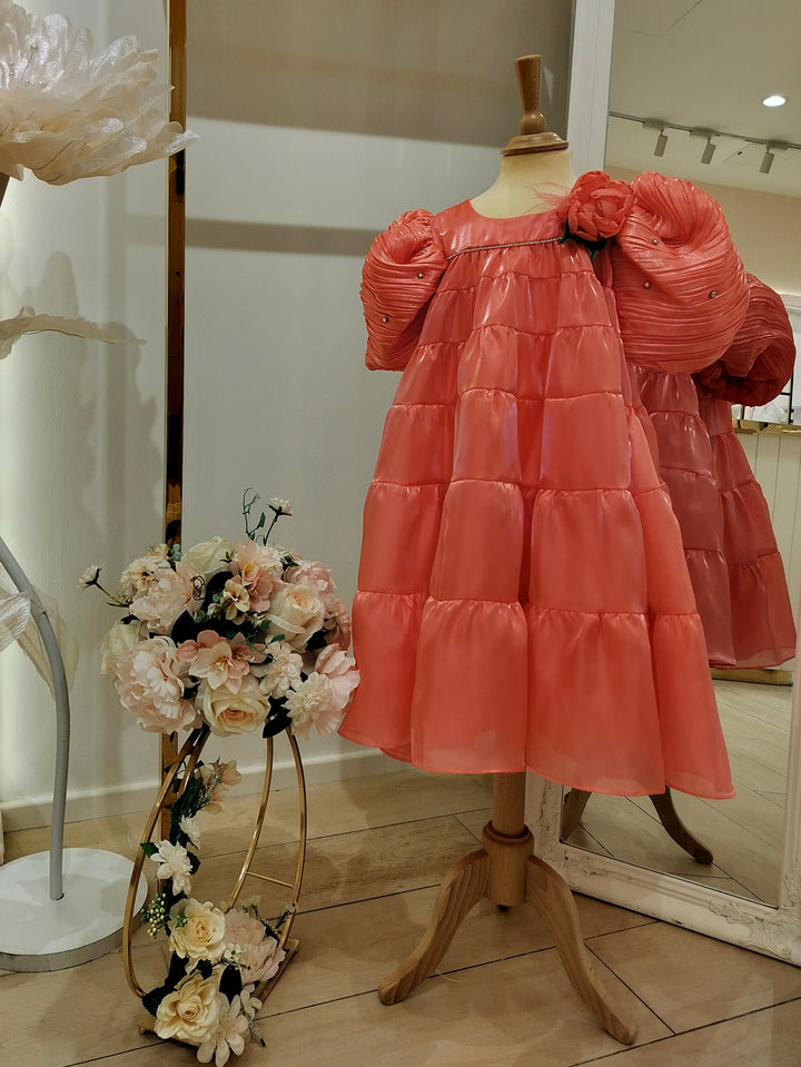 A pink girls' dress with floral print, displayed on a mannequin, accompanied by a small bouquet of flowers in front.