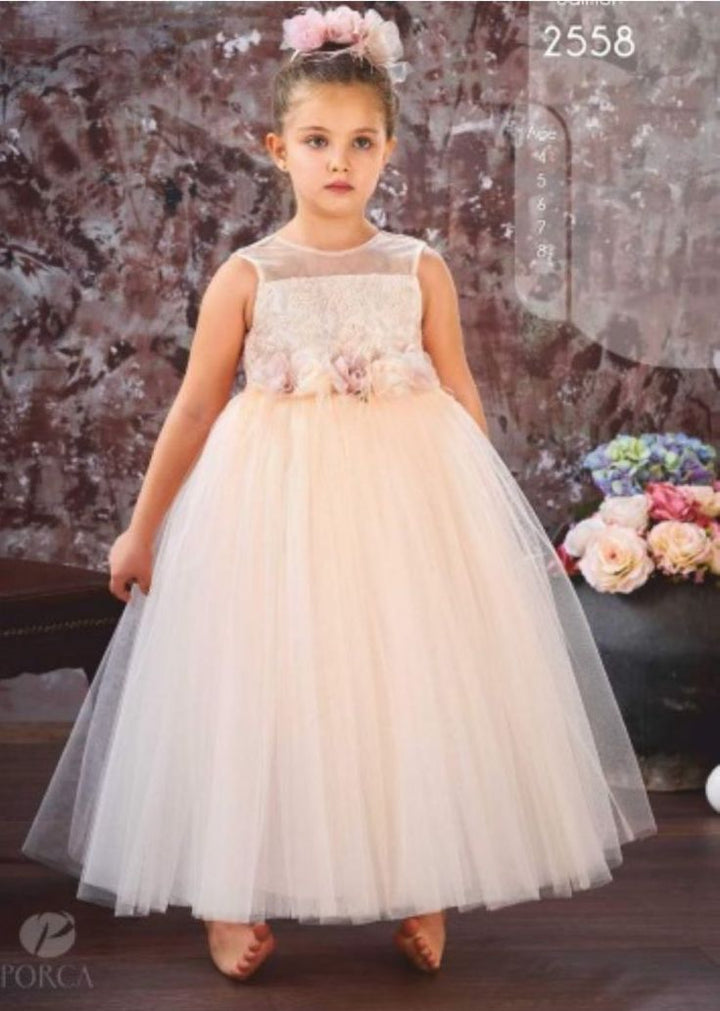 A young girl wearing a white floral A-line dress with 3/4 sleeves and a bow accent on the waist, standing in a room with floral backdrop.